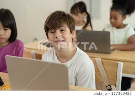 Smiling Caucasian Boy Learning with Laptop in a Diverse and Engaged Elementary Classroom in School Smiling Caucasian Boy Learning with Laptop in a Diverse and Engaged Elementary Classroom in School 117399483