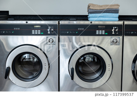Row of washing machines in self-service laundromat ready for use with neatly folded towels 117399537