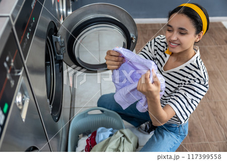Smiling woman managing household chores at public laundry 117399558