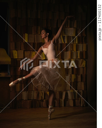 Ballerina in pointe shoes against a bookshelf. Ballet poses Ballerina in pointe shoes against a bookshelf. Ballet poses 117400132
