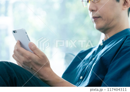 ソファに座ってスマホを操作する男性 ソファに座ってスマホを操作する男性 117404311