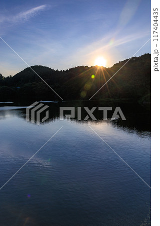 奈良市東部布目ダムの夏　ダム湖方向の夕景　対岸に沈んで行く夕日に照らされるダム湖の水面① 117404435