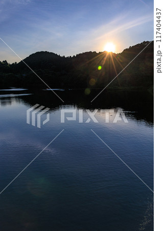 奈良市東部布目ダムの夏　ダム湖方向の夕景　対岸に沈んで行く夕日に照らされるダム湖の水面③ 117404437