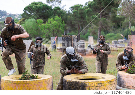 Men and women in protective uniform playing paintball on shooting range outdoor 117404480