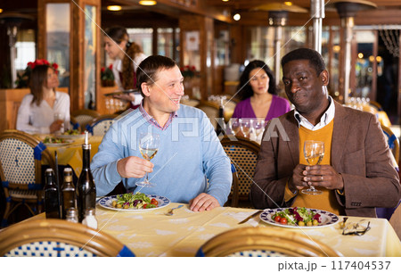 Two cheerful men having dinner in cozy restaurant 117404537