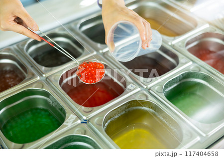 Hands scooping red bubble tea pearls into plastic cup Hands scooping red bubble tea pearls into plastic cup 117404658