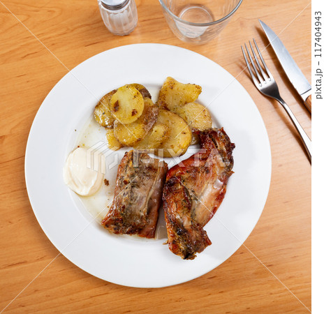 Lunch is served on plate - pieces of young rabbit cooked with segments of potato. Close-up 117404943