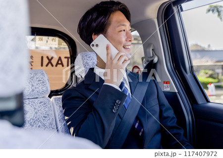タクシーの後部座席に座りスマホで話すビジネスマン 117407972