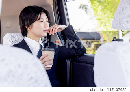 タクシーの後部座席に座りコーヒーを飲むビジネスウーマン 117407982