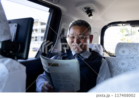 タクシーの後部座席で英字新聞を読む中高年ビジネスマン タクシーの後部座席で英字新聞を読む中高年ビジネスマン 117408002