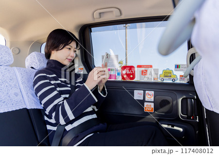 タクシーの後部座席でスマホを使う若い女性 117408012