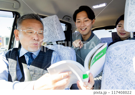 旅行先のタクシー内でガイドブックを見せて行き先を伝えるカップル  旅行先のタクシー内でガイドブックを見せて行き先を伝えるカップル  117408022