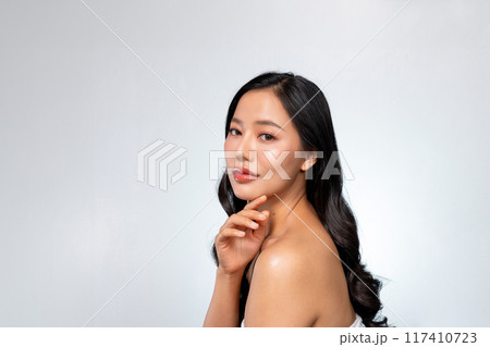 Elegant Asian woman poses against a grey background, looking at the camera while touching her chin. 117410723
