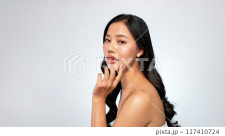 Elegant Asian woman poses against a grey background, looking at the camera while touching her chin. Elegant Asian woman poses against a grey background, looking at the camera while touching her chin. 117410724