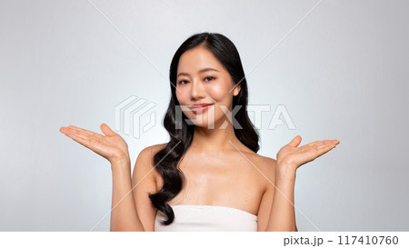An Asian beauty model poses with her palm open against a grey background, smiling at the camera. 117410760