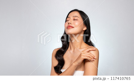 A young Asian woman with a perfect face poses, touching her shoulders with her eyes closed. A young Asian woman with a perfect face poses, touching her shoulders with her eyes closed. 117410765