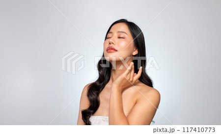 A young Asian beauty poses against a grey background, gently touching her face with her eyes closed. A young Asian beauty poses against a grey background, gently touching her face with her eyes closed. 117410773
