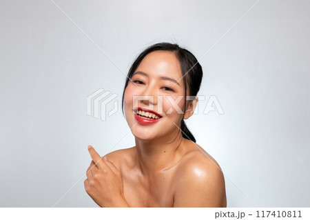 A pretty Asian woman smiles with her teeth visible while posing against a grey studio background. A pretty Asian woman smiles with her teeth visible while posing against a grey studio background. 117410811