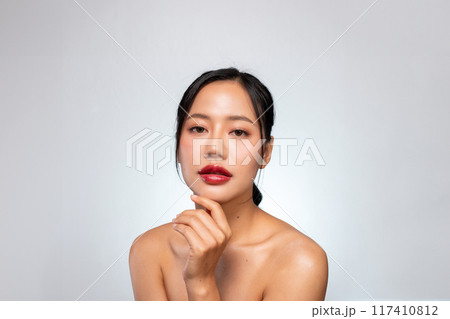 A beautiful Asian woman with red lips, and tanned skin poses against an isolated grey background. 117410812