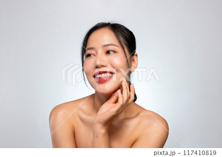 A pretty Asian woman poses against a grey studio background, smiles with her teeth visible. A pretty Asian woman poses against a grey studio background, smiles with her teeth visible. 117410819
