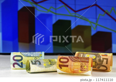 Against the background of the graphic chart are curled into a cylinder euro banknotes Against the background of the graphic chart are curled into a cylinder euro banknotes 117411110