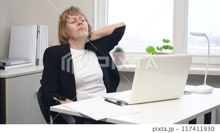 A female office worker stretches her stiff neck A female office worker stretches her stiff neck 117411930