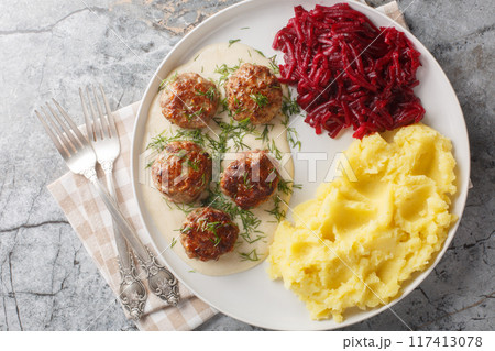Traditional meatballs with creamy sauce garnished with mashed potatoes and beets close-up in a plate. Horizontal top view Traditional meatballs with creamy sauce garnished with mashed potatoes and beets close-up in a plate. Horizontal top view 117413078