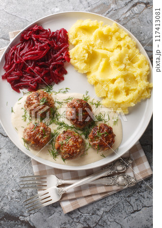 Portion of meatballs with creamy sauce with mashed potatoes and beet salad close-up in a plate on the table. Vertical top view 117413081