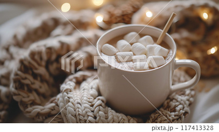 Cozy room decor with knitted blanket and a cup of hot cocoa with marshmallow on top and decorated lightings in white color tone. AI generated. 117413328