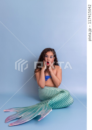 surprised girl in mermaid costume sitting on blue background 117415042
