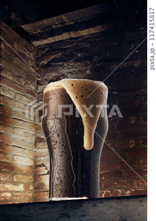Glass of cold, craft, dark beer with thick foam head, condensation on glass against rustic brick wall. Glass of cold, craft, dark beer with thick foam head, condensation on glass against rustic brick wall. 117415817