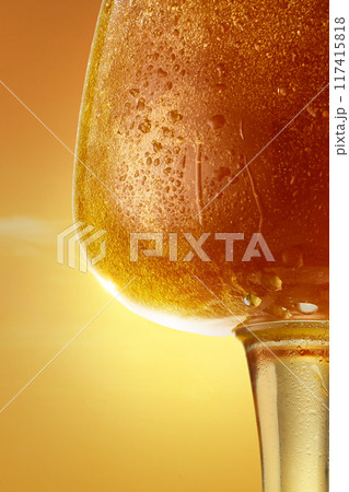 Close-up of glass filled with amber beverage, covered in condensation droplets against warm golden light background. Close-up of glass filled with amber beverage, covered in condensation droplets against warm golden light background. 117415818