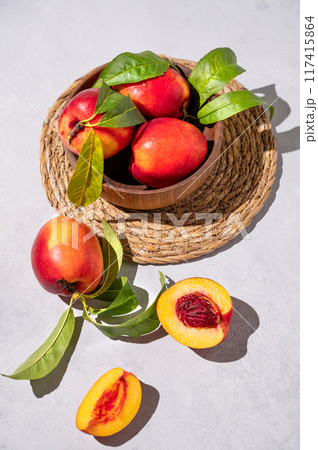 Juicy and sweet nectarines in a bowl on a light background with shadow. Healthy farm fruit concept. 117415864