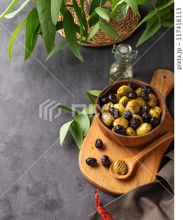 A set of green and black dried olives in bowl on a wooden cutting board on a dark background  117416113