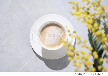 A spring bouquet with yellow mimosa flowers over a cup of coffee  cappuccino on a light background  117416142