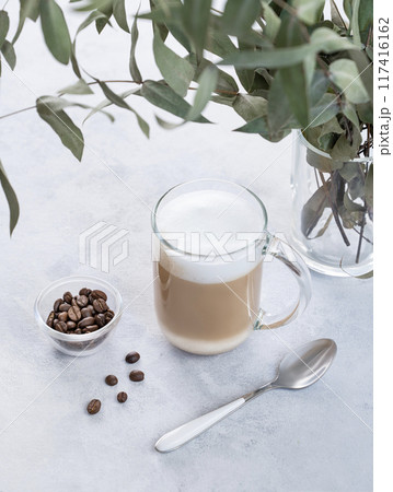 Cappuccino or latte with milk foam in glass on a light background with coffee beans  117416162