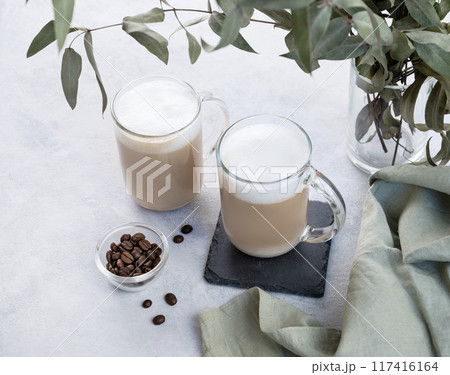 Two cappuccino or latte with milk foam in glasses on a light background with coffee beans Two cappuccino or latte with milk foam in glasses on a light background with coffee beans 117416164