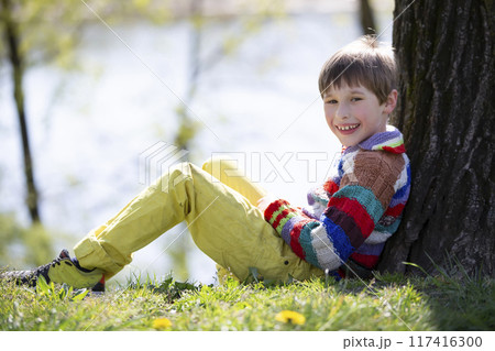 The child is sitting on the grass. Happy boy on a walk in the park. The child is sitting on the grass. Happy boy on a walk in the park. 117416300