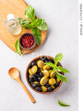 A set of green and black dried olives in wooden  bowl on a light background with olive oil and basil 117416460