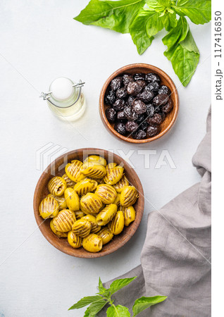 A set of green grill and black dried olives in wooden  bowls on a light background with olive oil 117416850