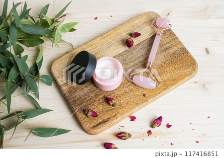 Face cream and massager on a wooden table. The concept of care cosmetics with rose and eucalyptus 117416851