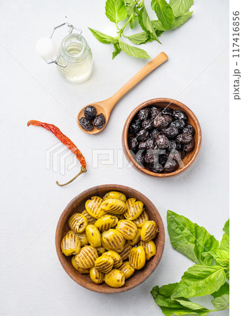 A set of green grill and black dried olives in wooden  bowls on a light background with olive oil  117416856