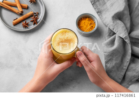 Hands holding turmeric golden milk latte with spices and honey. Detox, immunity boosting 117416861