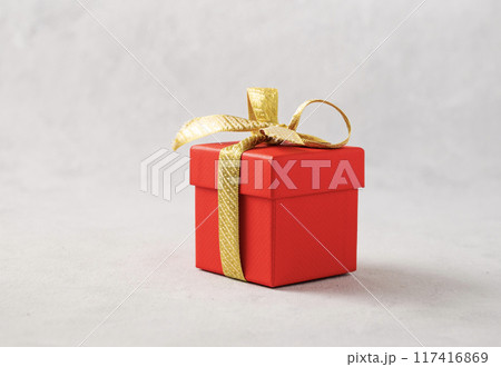 A red gift box with a gold ribbon on a gray background. The concept of holiday photography A red gift box with a gold ribbon on a gray background. The concept of holiday photography 117416869