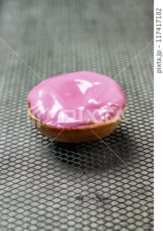 A pink frosted mini doughnut sits on a metal surface A pink frosted mini doughnut sits on a metal surface 117417182