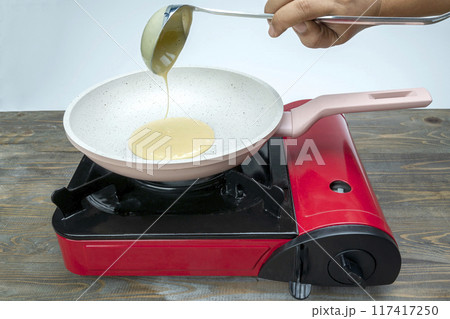 A person is cooking food in a pan on a stove 117417250