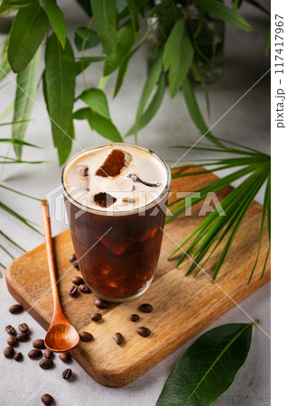 Iced coffee brew in a glass on a wooden board on a light background with coffee beans Iced coffee brew in a glass on a wooden board on a light background with coffee beans 117417967