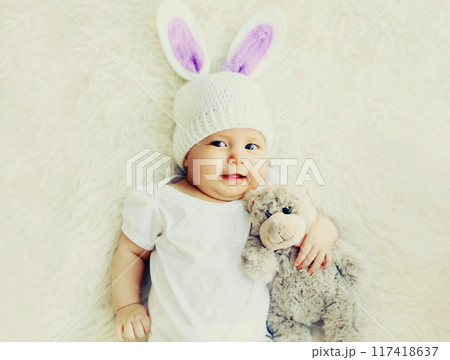 Close up portrait of sweet baby sleeping with teddy bear toy on a white bed at home 117418637