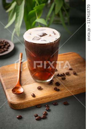 Iced coffee brew in a glass on a wooden board on a green background with coffee beans  117418770