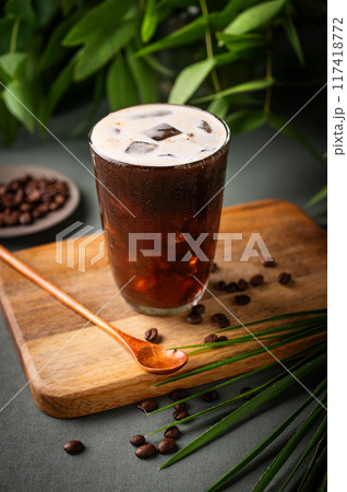 Iced coffee brew in a glass on a wooden board on a green background with coffee beans  117418772